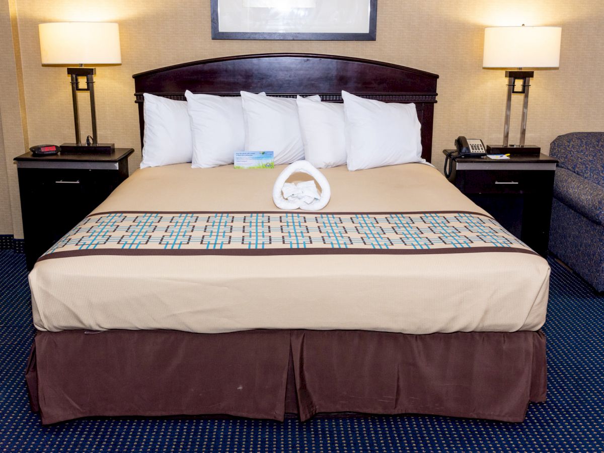 A neatly made bed with five pillows, folded towels, and two lamps on side tables in a hotel room.