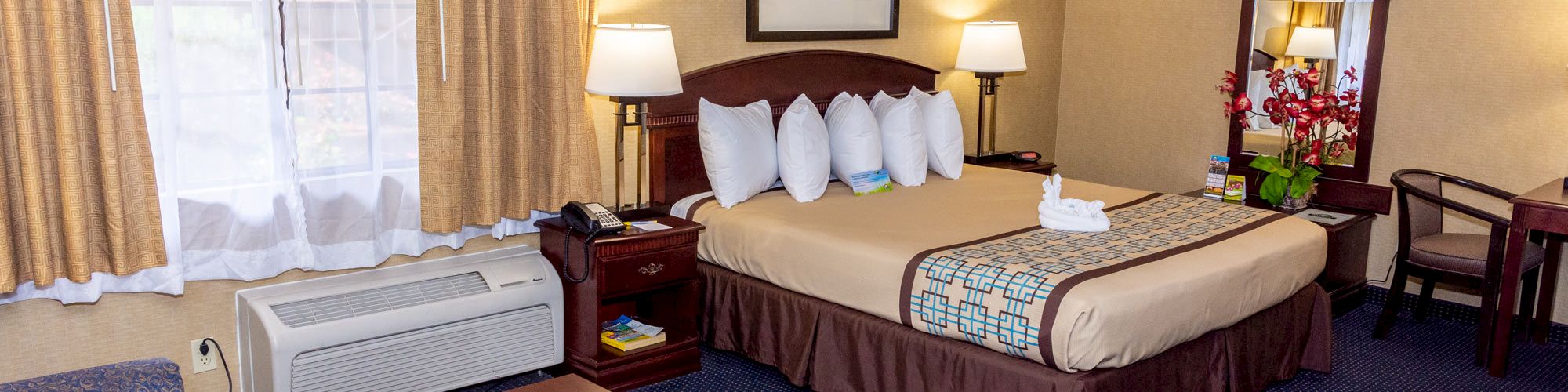 This is a photo of a hotel room with a bed, sofa, coffee table, desk, and an air conditioner near the window, ending the sentence.