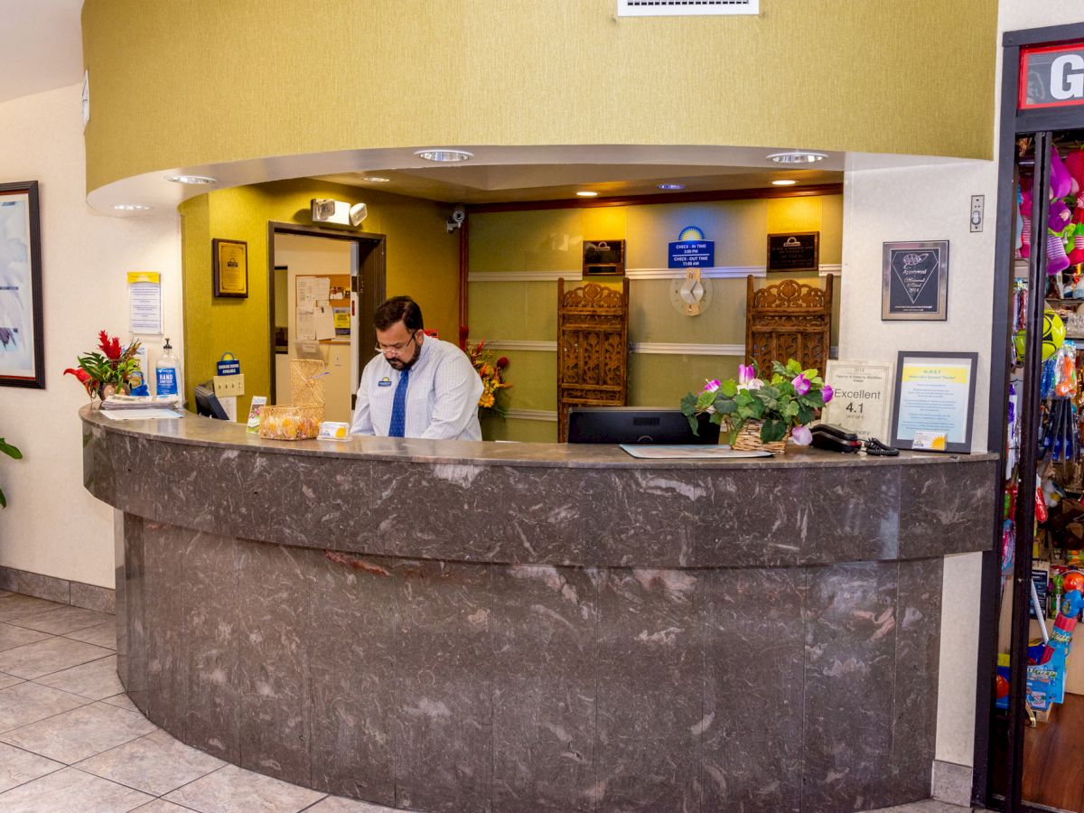 A hotel reception desk with a person working behind the counter, surrounded by flowers and various items, next to a gift shop.