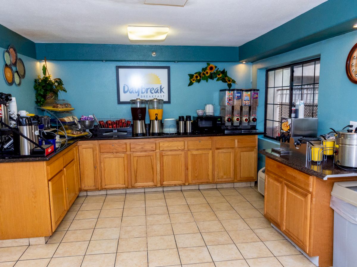 A breakfast area with coffee machines, cereal dispensers, and a variety of food items set on wooden cabinets. The wall sign reads 