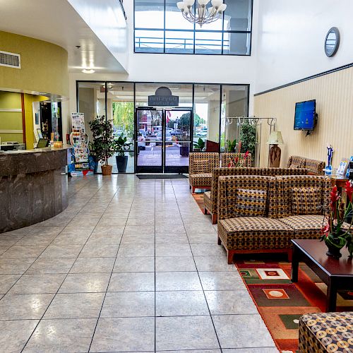 The image shows a hotel lobby with a check-in desk, seating area, plants, a TV, tiled flooring, and natural light from large windows ending the sentence.