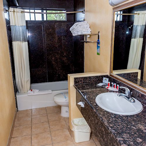 A bathroom with a sink, mirror, toilet, and shower/tub combo with a curtain. There are towels above the toilet and toiletries on the sink.