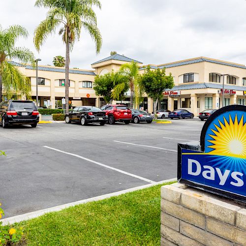 This image shows the parking lot of a Days Inn hotel, with several cars parked and the building visible in the background amidst palm trees.