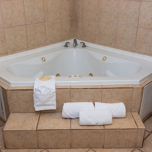 This image shows a corner jacuzzi bathtub with clean towels on the steps in front of it, and a plant in the right corner.