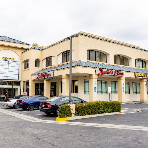 The image shows a beige multi-unit commercial building with a parking lot in front, housing a barber shop and another business.