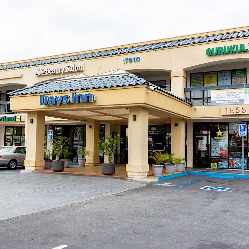 A commercial building with various businesses including a Days Inn hotel, beauty salon, and other shops, with cars parked outside.