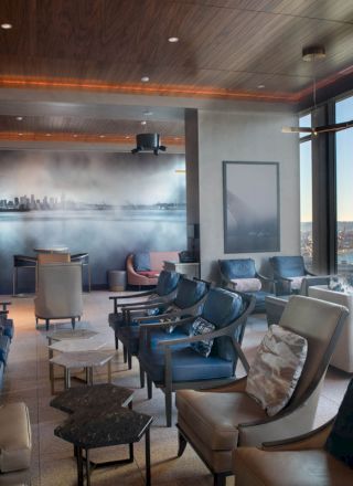A modern lounge with comfortable seating, large windows offering a scenic view of the waterfront and a wall mural of a cityscape in the background.