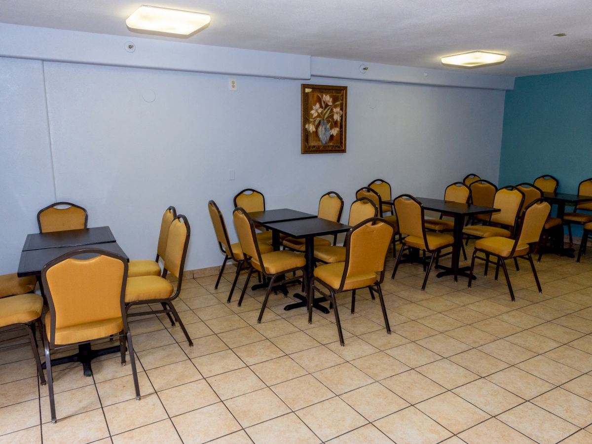 This image shows an empty dining area with several tables and chairs, a painting on the wall, and a tiled floor.